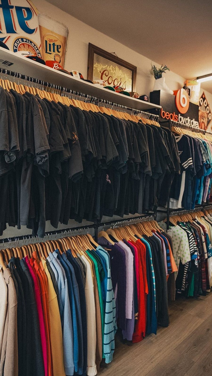 Long racks of vintage tees sorted by color with hats on the shelf above